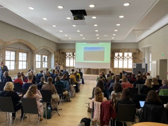 Viele Personen sitzen in einem großen Raum und schauen auf eine Präsentation.